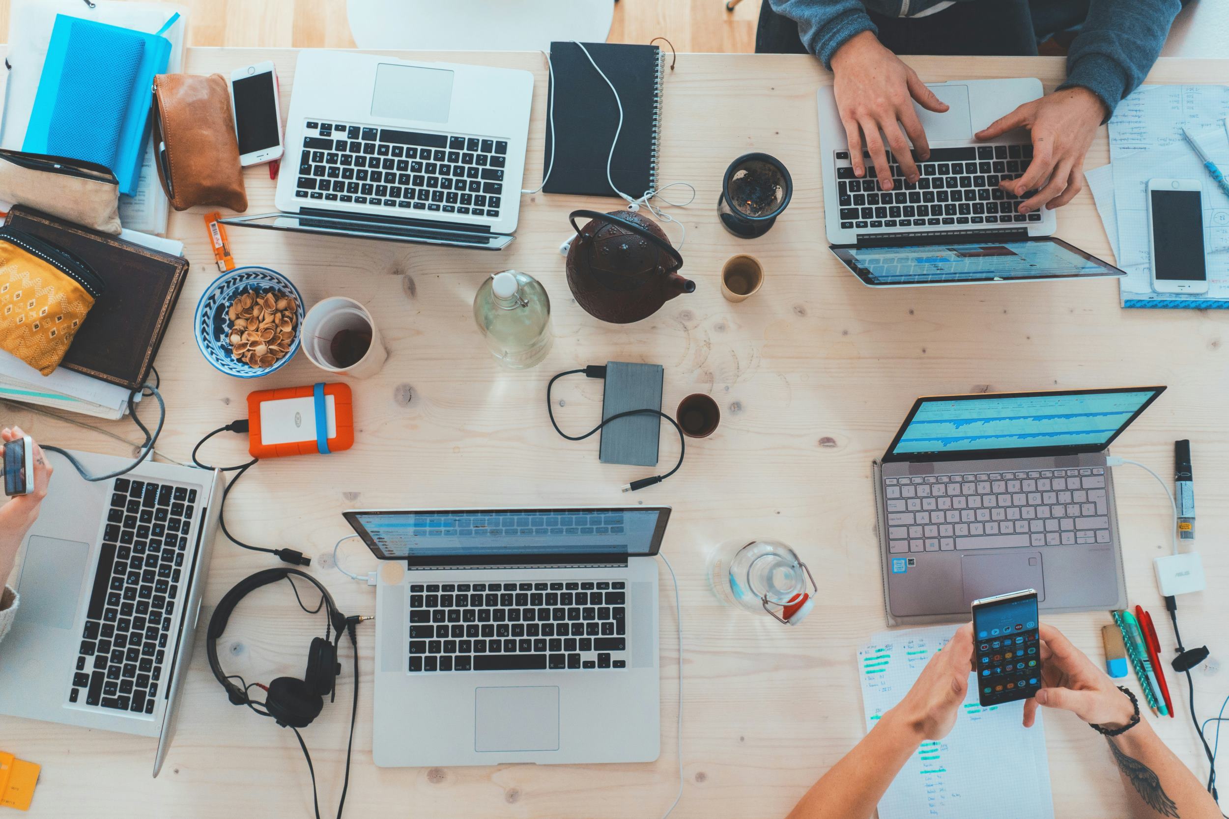 Overhead photo of multiple laptops and hands working on them.